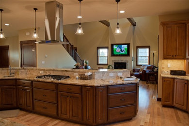 Exempel på ett stort amerikanskt kök, med luckor med upphöjd panel, granitbänkskiva, beige stänkskydd, stänkskydd i stenkakel, ljust trägolv, en dubbel diskho, skåp i mellenmörkt trä, rostfria vitvaror, en köksö och beiget golv