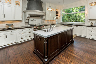 Inspiration for a large transitional galley dark wood floor and brown floor enclosed kitchen remodel in Richmond with a farmhouse sink, recessed-panel cabinets, white cabinets, soapstone countertops, gray backsplash, stone tile backsplash, stainless steel appliances and an island