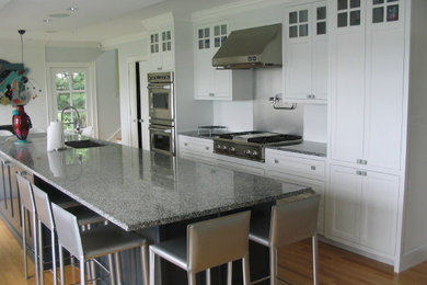 This is an example of a large classic galley enclosed kitchen in Boston with a submerged sink, recessed-panel cabinets, white cabinets, granite worktops, white splashback, stainless steel appliances, medium hardwood flooring and an island.