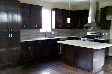 Large elegant l-shaped medium tone wood floor and brown floor open concept kitchen photo in Houston with a drop-in sink, raised-panel cabinets, dark wood cabinets, gray backsplash, porcelain backsplash and an island