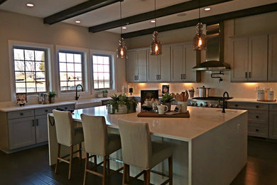 Cette image montre une cuisine américaine traditionnelle en L avec un évier de ferme, une crédence blanche, un électroménager en acier inoxydable, parquet foncé, îlot et un sol marron.