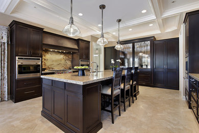 Enclosed kitchen - large tropical u-shaped ceramic tile and beige floor enclosed kitchen idea in Tampa with recessed-panel cabinets, dark wood cabinets, granite countertops, stainless steel appliances, an island, an undermount sink, beige backsplash and stone slab backsplash