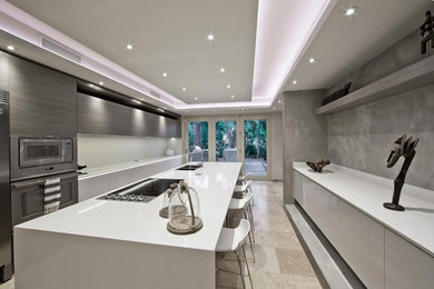 Large modern galley kitchen/diner in Miami with a double-bowl sink, flat-panel cabinets, white cabinets, engineered stone countertops, white splashback, stainless steel appliances, marble flooring and an island.