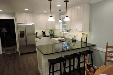 Mid-sized arts and crafts u-shaped dark wood floor eat-in kitchen photo in Other with a farmhouse sink, shaker cabinets, white cabinets, solid surface countertops, white backsplash, subway tile backsplash and stainless steel appliances