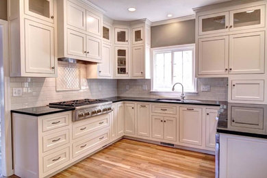 Example of a mid-sized transitional u-shaped light wood floor enclosed kitchen design in Boston with an undermount sink, beaded inset cabinets, white cabinets, granite countertops, white backsplash, subway tile backsplash, stainless steel appliances and a peninsula