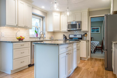 Example of a large transitional u-shaped light wood floor and brown floor eat-in kitchen design in New York with an undermount sink, recessed-panel cabinets, white cabinets, marble countertops, white backsplash, subway tile backsplash, stainless steel appliances, an island and gray countertops