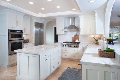 Inspiration for a mid-sized contemporary u-shaped limestone floor and beige floor enclosed kitchen remodel in San Diego with a farmhouse sink, shaker cabinets, white cabinets, quartzite countertops, white backsplash, ceramic backsplash, stainless steel appliances, an island and white countertops