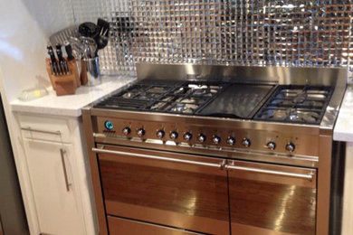 Example of a mid-sized trendy u-shaped dark wood floor open concept kitchen design in Dallas with an undermount sink, flat-panel cabinets, white cabinets, glass countertops, metallic backsplash, metal backsplash, stainless steel appliances and an island