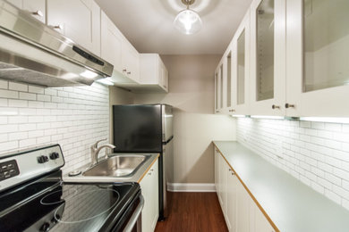 Mid-sized elegant galley dark wood floor and brown floor enclosed kitchen photo in DC Metro with a drop-in sink, shaker cabinets, white cabinets, solid surface countertops, white backsplash, subway tile backsplash, stainless steel appliances and no island
