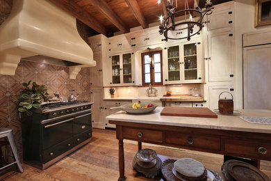 Example of a mid-sized mountain style single-wall medium tone wood floor and brown floor open concept kitchen design in Austin with a farmhouse sink, shaker cabinets, white cabinets, an island, limestone countertops, multicolored backsplash and ceramic backsplash