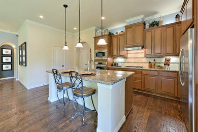 Kitchen - mid-sized traditional l-shaped medium tone wood floor kitchen idea in Chicago with raised-panel cabinets, medium tone wood cabinets, granite countertops, beige backsplash, stainless steel appliances and an island
