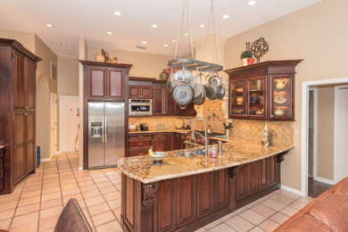 This is an example of a large traditional u-shaped open plan kitchen in Tampa with a double-bowl sink, raised-panel cabinets, dark wood cabinets, granite worktops, brown splashback, ceramic splashback, stainless steel appliances, terracotta flooring, a breakfast bar, beige floors and brown worktops.