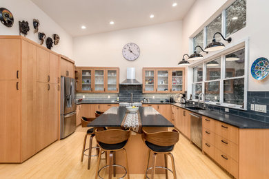 Example of a mid-sized trendy beige floor and vaulted ceiling eat-in kitchen design in Portland with an undermount sink, flat-panel cabinets, light wood cabinets, an island, black backsplash, ceramic backsplash, stainless steel appliances and black countertops