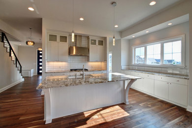 Moderne Küche mit flächenbündigen Schrankfronten, weißen Schränken, Granit-Arbeitsplatte, Küchenrückwand in Weiß, Rückwand aus Keramikfliesen, braunem Holzboden und Kücheninsel in Cleveland
