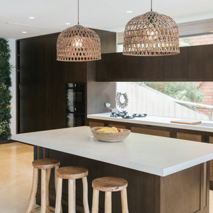 Photo of a tropical kitchen in Sydney with flat-panel cabinets, dark wood cabinets, window splashback, with island, beige floor and white benchtop.