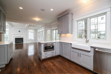 Mid-sized elegant u-shaped dark wood floor and brown floor eat-in kitchen photo in New York with a farmhouse sink, shaker cabinets, gray cabinets, quartz countertops, white backsplash, ceramic backsplash, stainless steel appliances and a peninsula