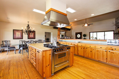 Example of a large mountain style u-shaped medium tone wood floor open concept kitchen design in Austin with flat-panel cabinets, medium tone wood cabinets, an island, wood countertops and black appliances