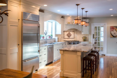 Photo of a large classic u-shaped kitchen/diner in Boston with a submerged sink, beaded cabinets, white cabinets, granite worktops, beige splashback, stainless steel appliances, light hardwood flooring, an island, stone tiled splashback and brown floors.