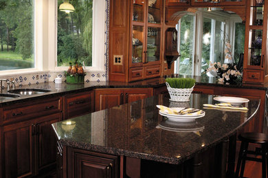 Eat-in kitchen - large traditional u-shaped medium tone wood floor eat-in kitchen idea in Chicago with a double-bowl sink, raised-panel cabinets, brown cabinets, granite countertops, beige backsplash, porcelain backsplash, paneled appliances and an island
