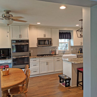 Mid-sized transitional eat-in kitchen designs - Inspiration for a mid-sized transitional galley vinyl floor and brown floor eat-in kitchen remodel in Baltimore with a farmhouse sink, shaker cabinets, white cabinets, granite countertops, gray backsplash, subway tile backsplash, stainless steel appliances, an island and multicolored countertops