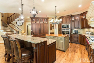 Example of a large classic u-shaped light wood floor and brown floor kitchen design in Raleigh with raised-panel cabinets, dark wood cabinets, granite countertops, beige backsplash, an island, beige countertops and an undermount sink