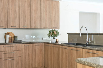 Cette image montre une cuisine minimaliste en bois clair de taille moyenne avec un évier 2 bacs, un plan de travail en quartz modifié, une crédence beige, une crédence en feuille de verre et un électroménager en acier inoxydable.