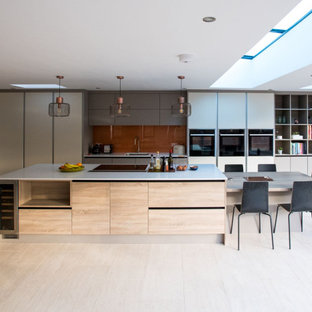 This is an example of an expansive contemporary galley kitchen in Hampshire with a submerged sink, flat-panel cabinets, grey cabinets, brown splashback, glass sheet splashback, integrated appliances, an island, beige floors and white worktops.