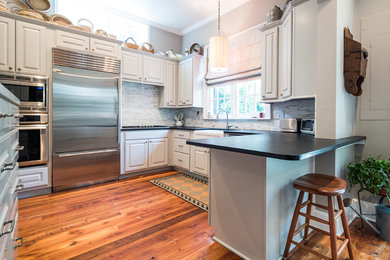 Inspiration for a mid-sized transitional u-shaped brown floor and medium tone wood floor enclosed kitchen remodel in Charleston with a farmhouse sink, raised-panel cabinets, white cabinets, soapstone countertops, gray backsplash, matchstick tile backsplash, stainless steel appliances and a peninsula