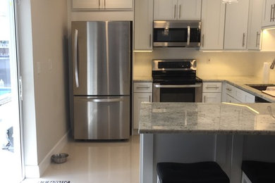 Inspiration for a mid-sized contemporary u-shaped porcelain tile and white floor eat-in kitchen remodel in Miami with an undermount sink, shaker cabinets, white cabinets, quartz countertops, white backsplash, subway tile backsplash, stainless steel appliances, a peninsula and white countertops