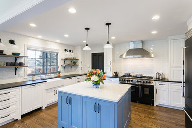 Example of a large classic u-shaped dark wood floor and brown floor eat-in kitchen design in Other with an island, a farmhouse sink, shaker cabinets, granite countertops, white backsplash, ceramic backsplash, paneled appliances and white countertops