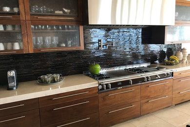 Inspiration for a large modern l-shaped ceramic tile and beige floor open concept kitchen remodel in Orange County with an undermount sink, flat-panel cabinets, medium tone wood cabinets, granite countertops, black backsplash, glass tile backsplash, stainless steel appliances and an island