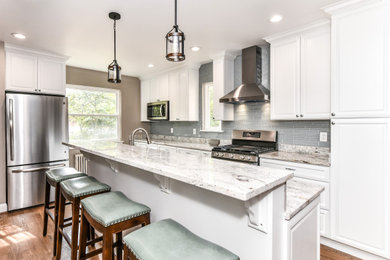 Example of a large minimalist l-shaped medium tone wood floor and brown floor eat-in kitchen design in DC Metro with a double-bowl sink, raised-panel cabinets, white cabinets, granite countertops, blue backsplash, glass tile backsplash, stainless steel appliances, an island and gray countertops
