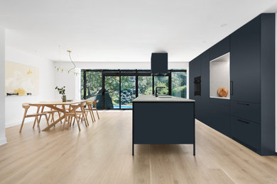 Example of a large minimalist galley light wood floor eat-in kitchen design in Montreal with an undermount sink, flat-panel cabinets, blue cabinets, quartz countertops, gray backsplash, quartz backsplash, paneled appliances, an island and gray countertops