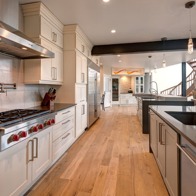 Open concept kitchen - transitional galley medium tone wood floor and brown floor open concept kitchen idea in Denver with a double-bowl sink, shaker cabinets, white cabinets, quartz countertops, beige backsplash, stone tile backsplash, stainless steel appliances and two islands