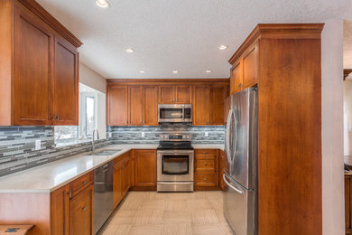 Eat-in kitchen - traditional eat-in kitchen idea in Calgary with an undermount sink, shaker cabinets, medium tone wood cabinets, gray backsplash, mosaic tile backsplash, stainless steel appliances and an island