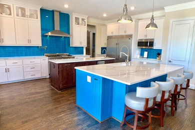 Expansive modern l-shaped kitchen/diner in Dallas with a submerged sink, shaker cabinets, white cabinets, engineered stone countertops, blue splashback, glass tiled splashback, stainless steel appliances, dark hardwood flooring, multiple islands, brown floors and white worktops.