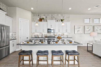 Example of a mid-sized trendy l-shaped medium tone wood floor and brown floor eat-in kitchen design in Dallas with a triple-bowl sink, recessed-panel cabinets, white cabinets, solid surface countertops, multicolored backsplash, ceramic backsplash, stainless steel appliances, an island and gray countertops