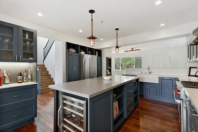 Example of a mid-sized trendy medium tone wood floor eat-in kitchen design in San Francisco with a farmhouse sink, shaker cabinets, blue cabinets, quartz countertops, white backsplash, ceramic backsplash, stainless steel appliances and an island