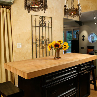 Mittelgroße Klassische Wohnküche in L-Form mit Landhausspüle, Schrankfronten mit vertiefter Füllung, schwarzen Schränken, Arbeitsplatte aus Holz, Küchenrückwand in Beige, Rückwand aus Steinfliesen, Elektrogeräten mit Frontblende, Korkboden und Kücheninsel in Detroit