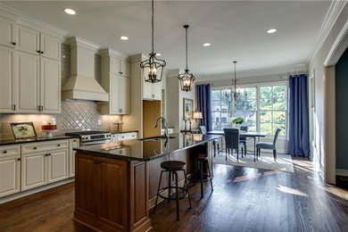 Inspiration for a mid-sized timeless galley dark wood floor eat-in kitchen remodel in Raleigh with an undermount sink, raised-panel cabinets, beige cabinets, granite countertops, gray backsplash, ceramic backsplash, stainless steel appliances and an island