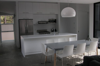 Example of a small minimalist galley concrete floor eat-in kitchen design in Other with an undermount sink, flat-panel cabinets, white cabinets, quartz countertops, white backsplash, stainless steel appliances and an island
