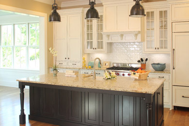 Eat-in kitchen - large traditional l-shaped medium tone wood floor and brown floor eat-in kitchen idea in Charleston with glass-front cabinets, white cabinets, granite countertops, beige backsplash, subway tile backsplash, paneled appliances, a farmhouse sink and an island