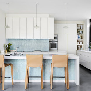 Contemporary u-shaped kitchen in Sydney with an undermount sink, flat-panel cabinets, white cabinets, blue splashback, white appliances, a peninsula, grey floor and white benchtop.