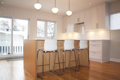 Example of a large trendy u-shaped light wood floor kitchen design in Montreal with an undermount sink, shaker cabinets, white cabinets, quartzite countertops, white backsplash, ceramic backsplash, stainless steel appliances and an island