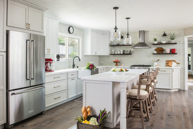 Inspiration for a country l-shaped kitchen in San Francisco with a belfast sink, recessed-panel cabinets, white cabinets, grey splashback, metro tiled splashback, stainless steel appliances, dark hardwood flooring, an island, brown floors and white worktops.