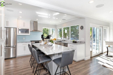 Example of a mid-sized trendy l-shaped medium tone wood floor and brown floor eat-in kitchen design in San Francisco with a farmhouse sink, shaker cabinets, white cabinets, quartzite countertops, blue backsplash, ceramic backsplash, stainless steel appliances, an island and gray countertops
