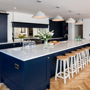 Large classic single-wall kitchen in Berkshire with a double-bowl sink, recessed-panel cabinets, blue cabinets, mirror splashback, light hardwood flooring, an island and beige floors.