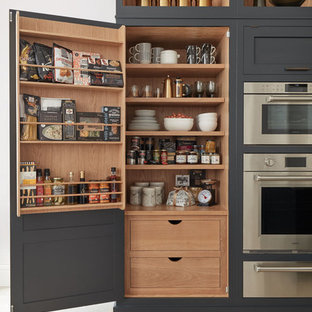 Exemple d'une cuisine ouverte linéaire tendance avec un évier de ferme, un placard à porte shaker, des portes de placard noires, un plan de travail en quartz, une crédence blanche, une crédence en marbre, un électroménager en acier inoxydable, un sol en calcaire, un îlot central, un sol beige et un plan de travail blanc.