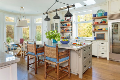 Photo of a country single-wall kitchen/diner in Los Angeles with a belfast sink, stainless steel appliances, medium hardwood flooring, an island, brown floors, recessed-panel cabinets and white cabinets.