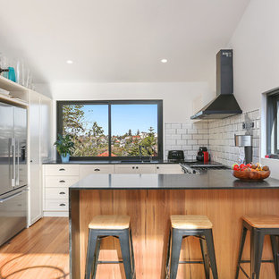 Contemporary u-shaped kitchen in Sydney with a double-bowl sink, shaker cabinets, white cabinets, white splashback, subway tile splashback, stainless steel appliances, light hardwood floors, a peninsula and black benchtop.